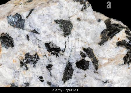 Pegmatitgranit aus Zentral-Arizona. Große schwarze Biotit-Glimmer-Kristalle gegen weißen Quarz. Fotografiert auf schwarzem Hintergrund. Stockfoto