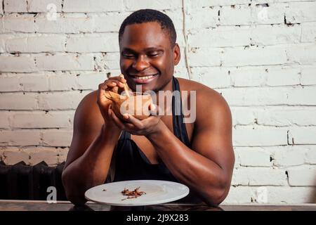 Ein junger und selbstbewusster afroamerikanischer Mann in einer schwarzen Schürze modelliert einen Töpfer aus einer Tonwarenwerkstatt. Tontopf in der Hand des lateinischen Künstlers Stockfoto