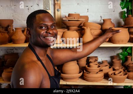 Happy dunkelhäutig afroamerikanischen Geschäftsmann Töpfer Mann Formen in der Werkstatt. Bildhauer Töpferei Tontopf in einem Studio-Arbeitsplatz. Kreativität und Stockfoto