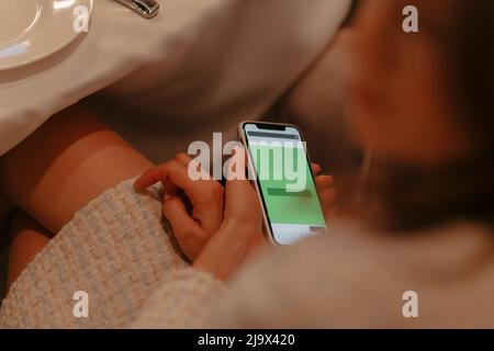 Mädchen, das Technologie und Smartphone-Konzept nutzt. Hand hält Handy mit grünem Hintergrund im Café. Für Text platzieren. Hochwertige Fotos Stockfoto