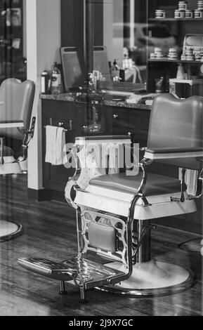 Retro-Friseurstuhl durch das Fenster des Friseursalons. Foto im Vintage-Stil in Schwarz und Weiß. Niemand, selektiver Fokus, Straßenfoto Stockfoto