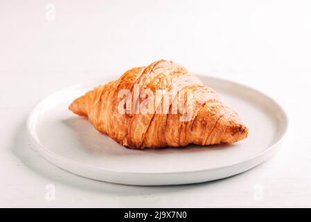 Teller mit einem frischen Croissant auf weißem Tisch. Stockfoto