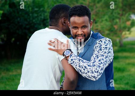 Zwei schwarze Männer in stilvollen Anzügen treffen sich in einem Sommerpark. Afroamerikanische Freunde hispanic Geschäftsmann umarmen Umarmung begrüßen einander Teamwork Stockfoto