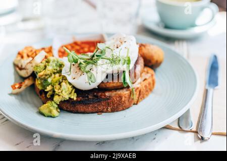 Gesundes Frühstück mit pochierten Eiern, gegrillten Halloumi, Rührei geräuchertem Harissa Tofu, zerschmetterner Avocado, gegrillten Pilzen und Tomatenbohnen auf Toast Stockfoto