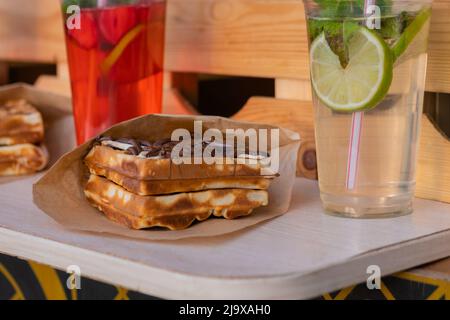 Wiener Waffeln mit Schokolade, Creme und Mojito-Cocktail auf dem Tisch - Nahaufnahme Stockfoto