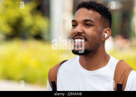 Fröhlicher junger Mann, der in Ohrhörern Musik hört und im Freien läuft Stockfoto