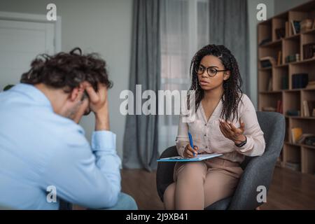 Serious junge afroamerikanische Dame Psychologin Beratung weinen deprimiert europäischen Mann in der Klinik Stockfoto