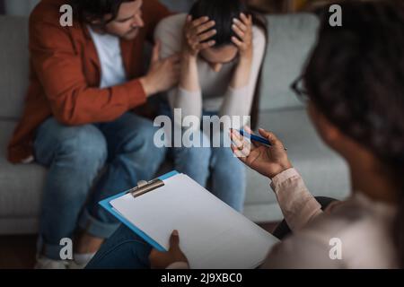 Unglücklicher junger europäischer Mann beruhigt weinende Frau und spricht mit dem Psychologen im Klinikinnern Stockfoto