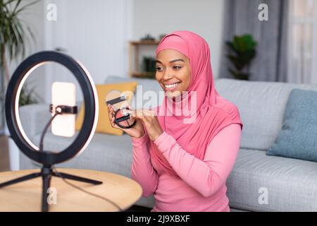 Happy muslim Beauty Blogger zeigt Make-up-Produkt und macht Überprüfung, im Gespräch mit Handy auf Ringlampe gesetzt Stockfoto