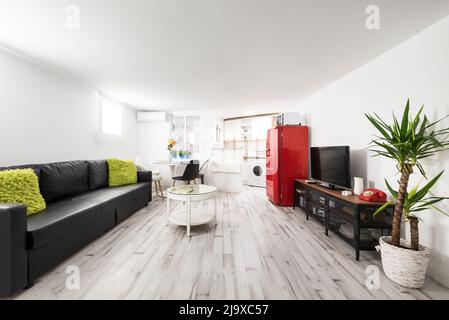 Studio-Apartment mit drei-Sitzer-Schlafsofa aus schwarzem Leder, offener Küche und rotem Vintage-Kühlschrank Stockfoto