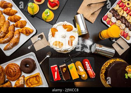 Dessert und Kuchen auf einem schwarzen Tisch, Cremeschokolade, Puderzucker, Buttercroissants, Orangensaft, Teekuchen, süße Schnecken. Stockfoto