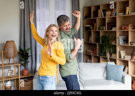 Positive Paar Mittleren Alters Tanzen Im Wohnzimmer Innenraum, Spaß Zusammen Haben Stockfoto