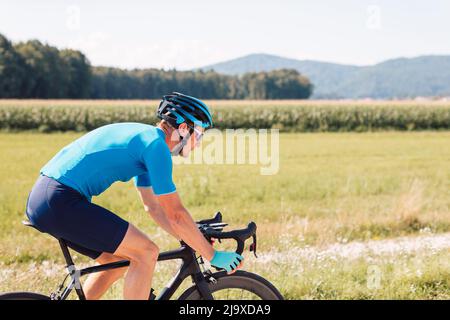 Seitenansicht eines kaukasischen Radfahrers, in blauer Sportbekleidung mit Helm und Sonnenbrille, auf einem Rennrad Stockfoto
