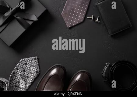 Klassische Herren Accessoires - Geschenk, Slipper Schuhe, Krawatte, Gürtel auf schwarzem Hintergrund. Grußkarte zum Happy Father's Day. Stockfoto