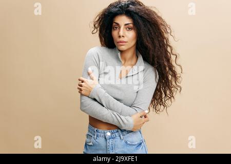 GUTES ANGEBOT. Selbstbewusste, seriöse, hübsche lateinische Hündin mit afro gefalteten Armen, überkreuzt die Hand, umarmt sich, lacht, bleibt isoliert über Gelb Stockfoto