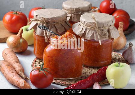 Hausgemachter Kaviar aus Äpfeln, Karotten, Paprika, Knoblauch und Tomaten in Gläsern auf hellgrauem Hintergrund Stockfoto