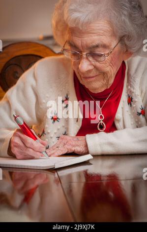 Ältere Frau, die an einem Tisch sitzt und einen Brief schreibt Stockfoto