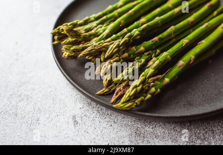 Nahaufnahme der Speere mit frischem Spargel auf dem Teller auf der grauen Theke. Stockfoto