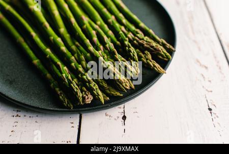 Nahaufnahme von Speeren mit frischem Spargel auf einem Teller auf dem weißen Tisch. Stockfoto