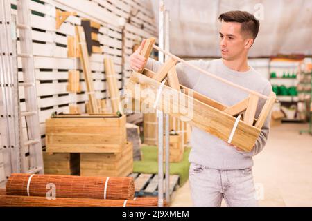 Junger Mann wählt hölzernen Blumentopf Stockfoto