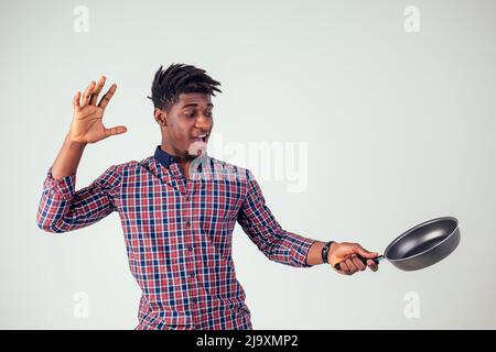 afroamerikanischer Koch kitchener hält eine Bratpfanne Zauberer Mann Kochen Magie fliegende Lebensmittel Salat, Karotte, Knoblauch, Zwiebel, Pfeffer, Kartoffel, Gurke Stockfoto