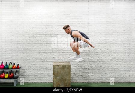Der junge Mann springt mitten in der Luft auf der Sportbox, die Arme reichen nach außen Stockfoto