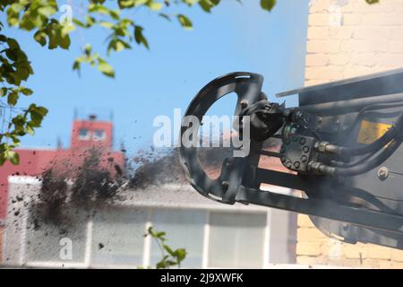 Das Straßenfräsfahrzeug lädt gefrästen Asphalt in einen Muldenkipper in einem engen Innenhof mit alten Häusern. Stockfoto
