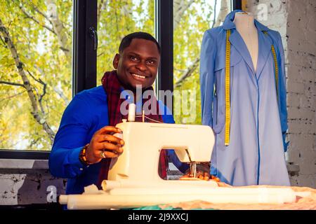 Porträt eines schönen afrikanischen Mann Näherin mit Nähmaschine.Afrio amerikanischer Mann stilvolle Designer arbeiten in Schneiderwerkstatt Schaufensterpuppe Mantel, Tisch Stockfoto