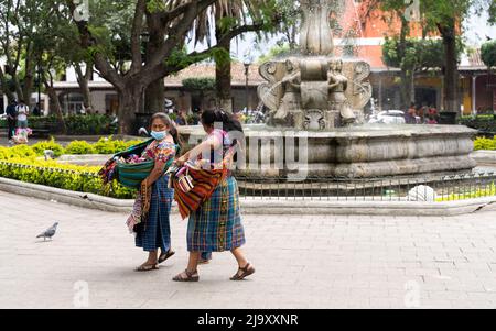 Zwei indigene Maya-Frauen, die Waren verkaufen, laufen auf dem Plaza Central Park in Antigua Guatemala Stockfoto