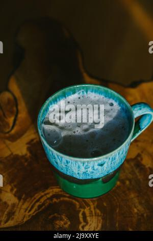 Ein schaumiger Latte in einem Keramikbecher sitzt auf einem Holztisch Stockfoto