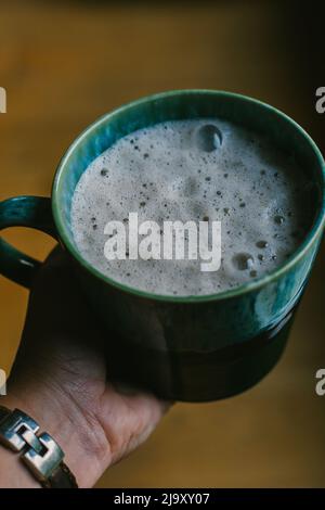 Ein schaumiiger Latte sitzt in der Handfläche Stockfoto