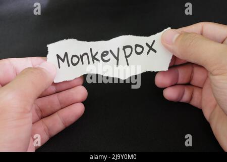 Konzept der Monkeypox-Viruserkrankung. Hand hält Papier mit Wort monkeypox auf schwarzem Hintergrund. Stockfoto