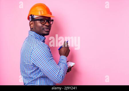 Schwarzer Mann afroamerikanischen schriftlich Ideen in einem Notizbuch malt die Wand in rosa Farbe. Glückliche afrikanische Baumeister im Haus, Geschäftsmann trägt ein Stockfoto