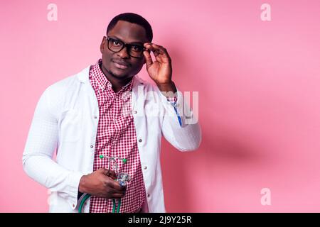 Glücklicher afrikanischer Chirurg Kardiologe Arzt in einem weißen Mantel auf einem rosa Hintergrund im Studio. Stockfoto