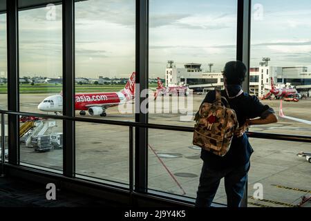 Ein inländischer Reisender beobachtet einen ankommenden Airbus A320-200 von Thai AirAsia (FD) vor einem inländischen Abflugsteig am Don Mueang International Airport (DMK) in Bangkok. Internationale Reisen nach Thailand und inländischer Tourismus im Land werden wieder aufgenommen, da die thailändische Regierung die Einreisebestimmungen im Rahmen ihres Thailand Pass-Programms vereinfacht, so dass internationale Reisende das Land ohne einen schnellen PCR-Test für COVID-19 oder Quarantäne bei der Ankunft betreten können. Die thailändische Regierung hat auch signalisiert, dass die Auflage, Gesichtsmasken im Freien zu tragen, voraussichtlich Mitte Juni 2022 enden wird. Stockfoto