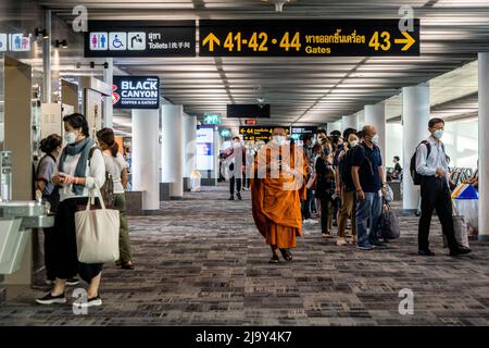 Ein buddhistischer Mönch mit Gesichtsmaske geht an einer Schlange von Menschen mit Gesichtsmasken vorbei, die an Bord eines Flugzeugs gehen, um vom internationalen Flughafen Don Mueang (DMK) in Bangkok abfliegen zu können. Internationale Reisen nach Thailand und inländischer Tourismus im Land werden wieder aufgenommen, da die thailändische Regierung die Einreisebestimmungen im Rahmen ihres Thailand Pass-Programms vereinfacht, so dass internationale Reisende das Land ohne einen schnellen PCR-Test für COVID-19 oder Quarantäne bei der Ankunft betreten können. Die thailändische Regierung hat auch signalisiert, dass die Auflage, Gesichtsmasken im Freien zu tragen, voraussichtlich Mitte Juni 2022 enden wird. Stockfoto