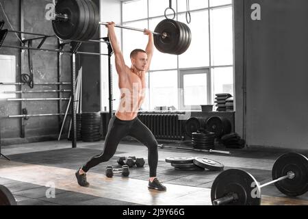 Mann trainiert mit schwerer Langhantel, die über den Kopf angehoben wird, und einer Bar im Fitnessstudio. Fitness-Studio Schwergewicht Hebe Bar durch starke Mann Training. Stockfoto