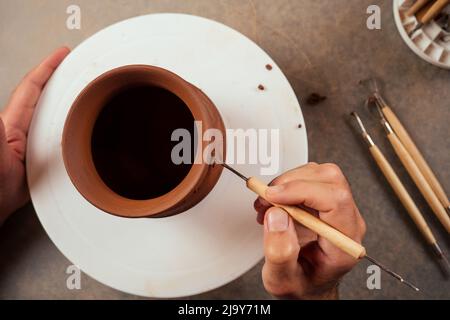 Nahaufnahme schmutziger Hände eines Mannes, einer Töpferin, die einen Tonerde-Krug auf dem Kreis des Töpfers im Werkstatt-Copyspace-Studio kreiert Stockfoto