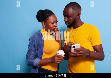 Schockierte Männer und Frauen, die unerwartete Nachrichten auf dem Smartphone lesen. Freundin deckt offenen mputth mit der Hand nach überrascht Reaktion, Blick auf Handy-Bildschirm. Betäubt Stockfoto
