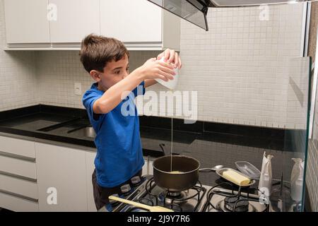 8-Jähriger in der Küche gießt Kondensmilch, um brigadeiro (Brigadier) zu machen. Stockfoto