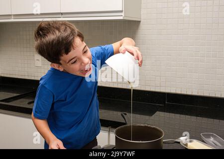 8-jähriges Kind gießt Kondensmilch in die Pfanne und versucht, sie zu essen. Stockfoto