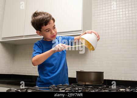 8-jähriges Kind gießt Kondensmilch in die Pfanne und versucht, sie zu essen. Stockfoto