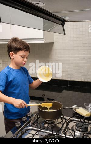 8-jähriges Kind gießt Kondensmilch in die Pfanne und versucht, es zu essen vertikales Foto. Stockfoto