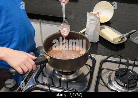 Kind mit einem Löffel, der die Textur von brigadeiro, einer brasilianischen Süßigkeit, überprüft. Stockfoto