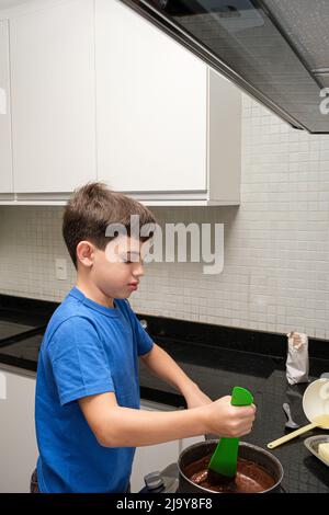 8-jähriges Kind in der Küche, das den brigadeiro mit einem Spachtel rührt. Eine brasilianische Süßigkeit. Stockfoto