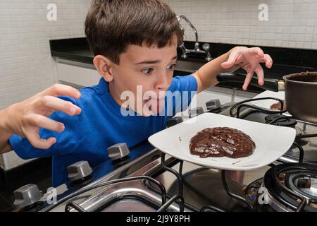 8-jähriges Kind vor einem Teller mit süßem brigadeiro und mit ausgestreckter Zunge. Stockfoto