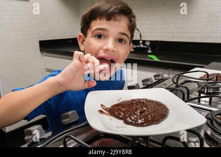 8-jähriges Kind vor einem Teller mit süßem brigadeiro und leckt seinen Finger. Stockfoto