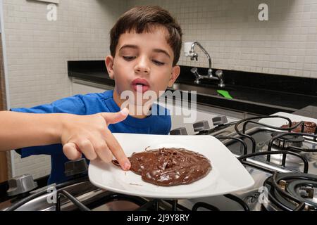 8-jähriges Kind, das seinen Finger mit dem süßen brigadeiro auf den Teller legt. Stockfoto