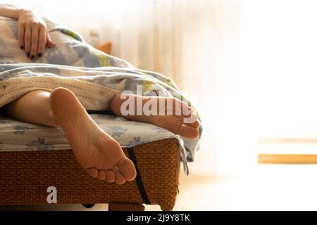 Mädchenbeine auf dem Bett in einer Decke zu Hause am Morgen schläft das Mädchen auf dem Bett, weibliche Beine, Ruhe, Sofa Stockfoto