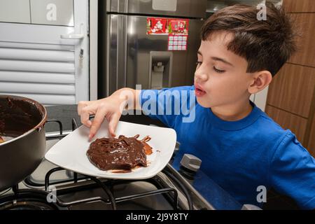 8-jähriges Kind, das mit den Fingern den brigadeiro, einen brasilianischen Süßen, abholt. Stockfoto